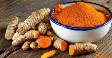 Bowl of turmeric powder next to fresh turmeric roots on a wooden surface.