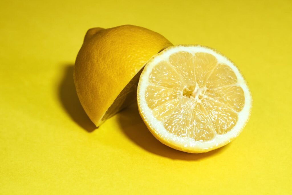 Whole lemon and a halved lemon on a yellow background, showcasing the fruit's bright color and texture.