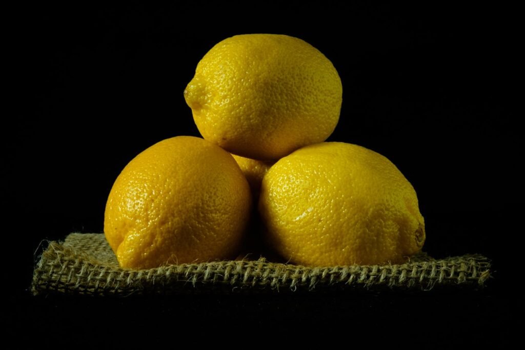 Three fresh yellow lemons stacked on a piece of burlap fabric against a black background.