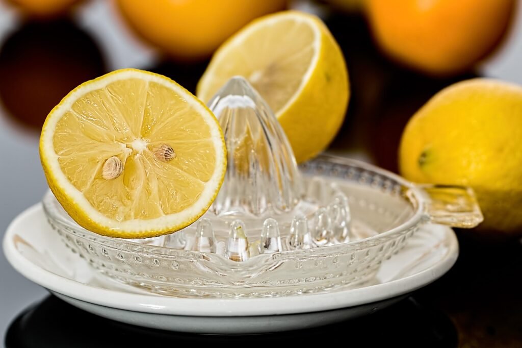 A glass lemon squeezer with a halved lemon placed on it, alongside whole lemons in the background.